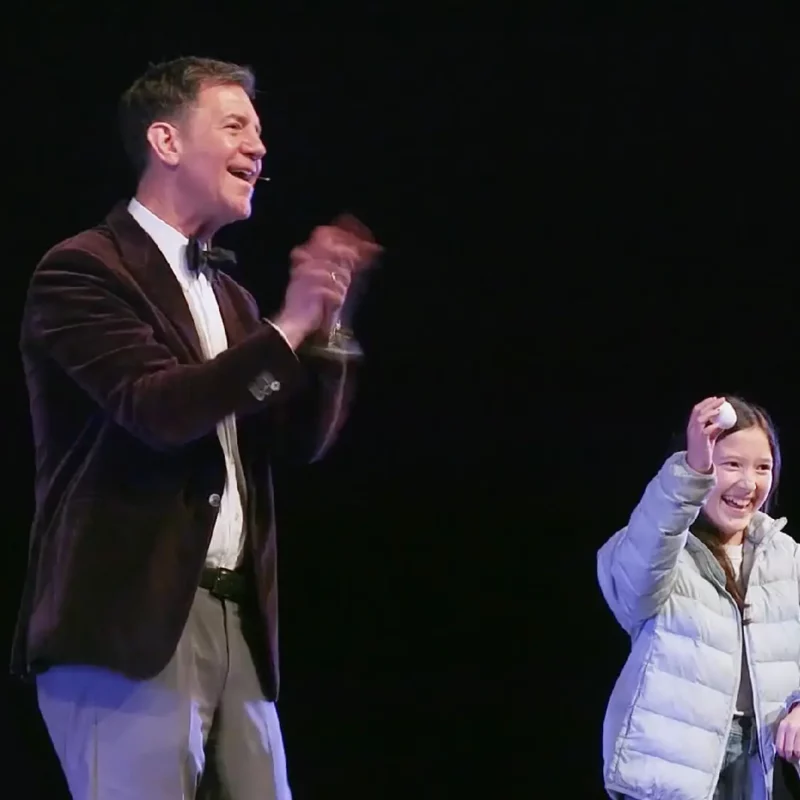 Doug performing with an audience volunteer. The volunteer smiles and holds an egg.